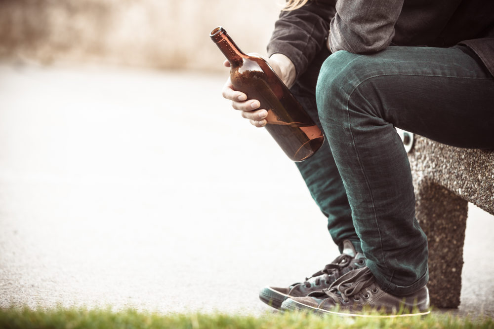 Man depressed with wine bottle sitting on bench outdoor
