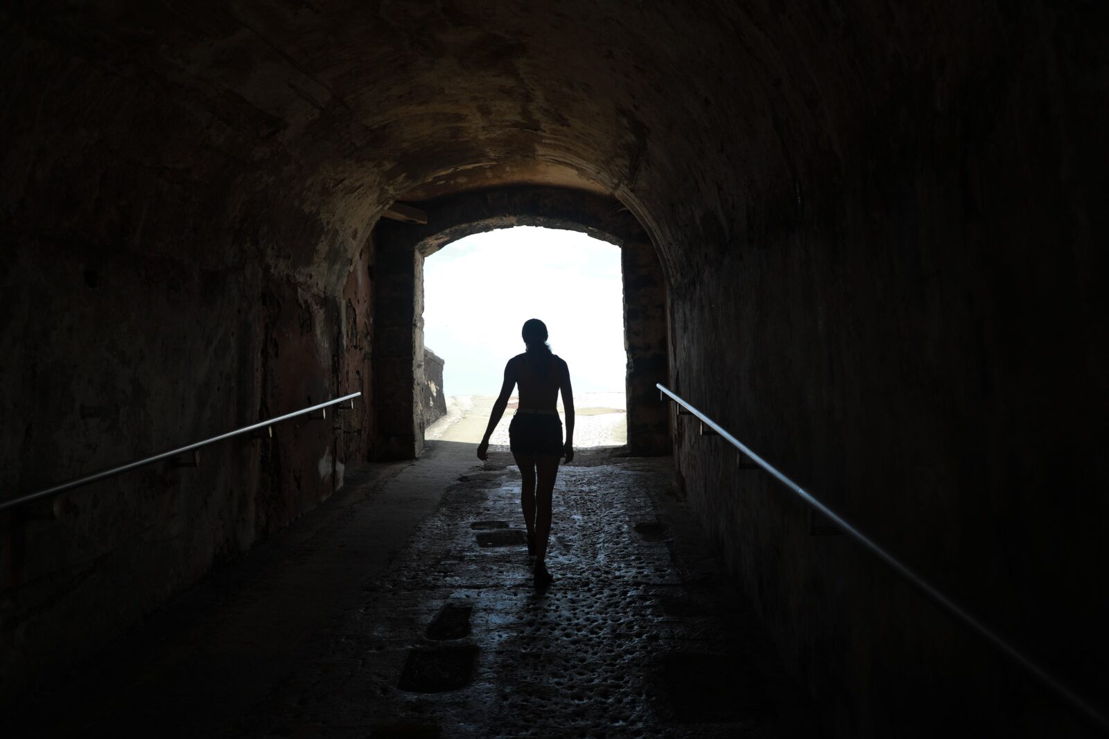 woman walks towards light at the end of a dark tunnel