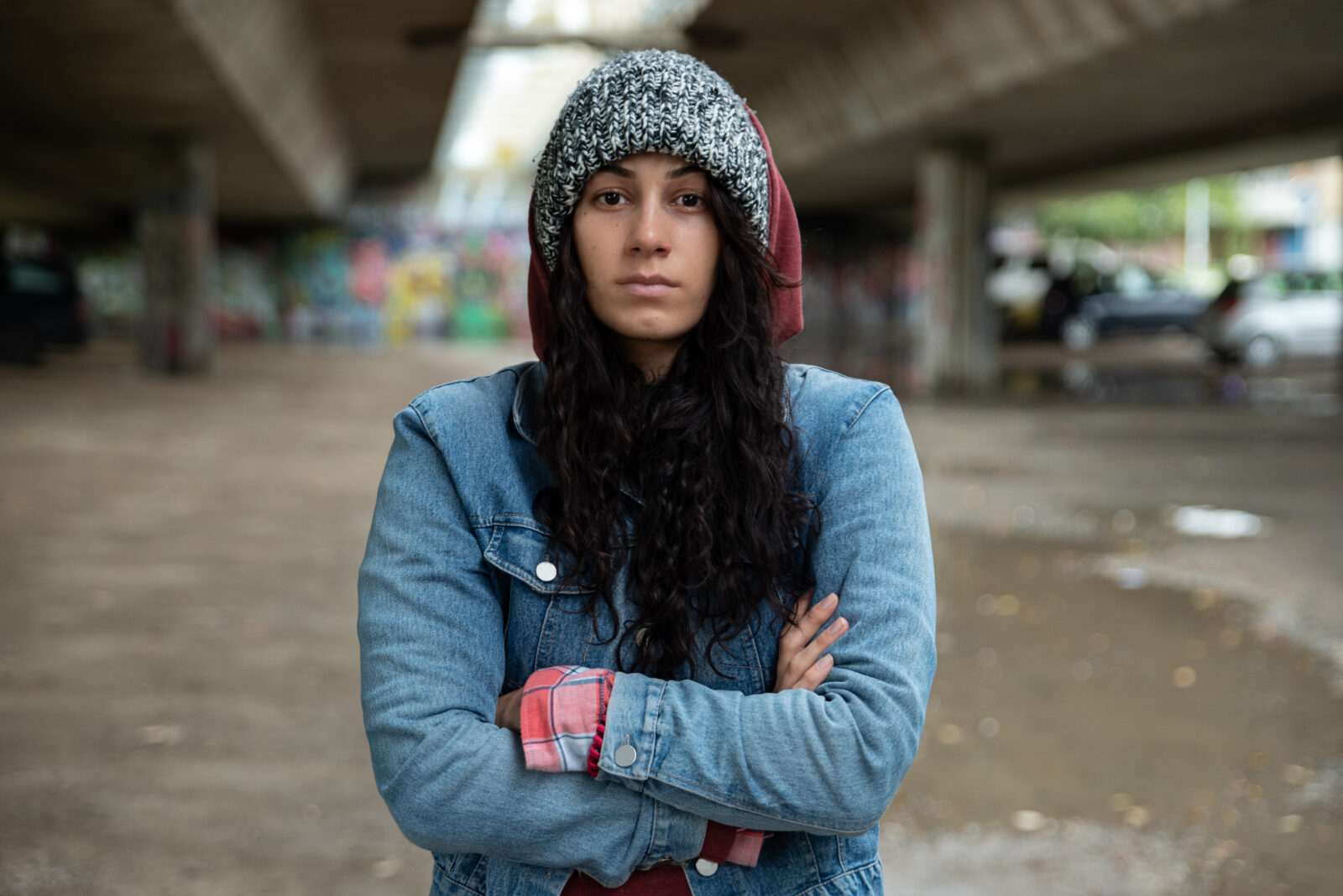 Young depressed homeless girl or woman standing alone under the bridge on the street on the cold weather feeling anxious abandoned and freezing selective focus