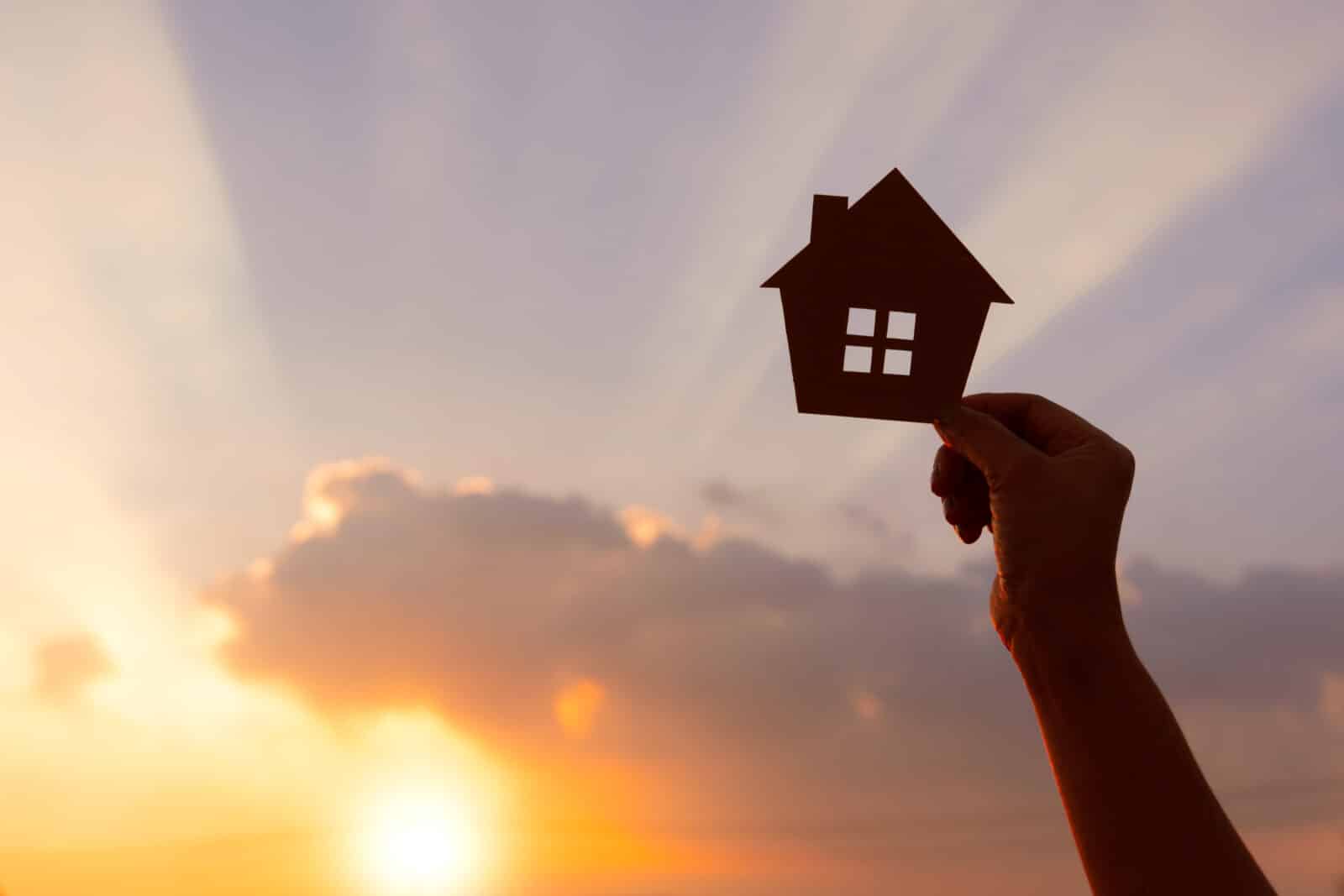 woman hands holding paper house on sunrise, family home, homeless housing, home protection insurance concept, international day of families, new life, foster home care, and real estate.